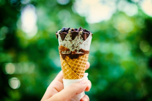 Hand holding ice cream on blurred natural green background, selective focus and added color filter