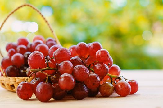 Red grape fruit in the basket on the wooden table with the natural blurred background