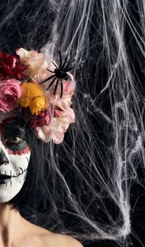 girl with black hair is dressed in a wreath of multi-colored roses and makeup is made on her face Sugar skull to the day of the Dead, close up