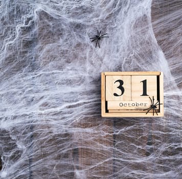 White spider web and wooden retro calendar made of blocks with the date of October 31, backdrop for Halloween holiday