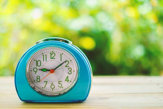 Old blue alarm clock on wooden table with blurred green natural background