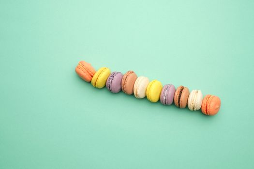round multi-colored baked macarons with cream lie in a line on a green background, flat lay, copy space 