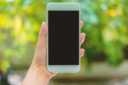 Hand holding mobile smartphone on blurred natural green background