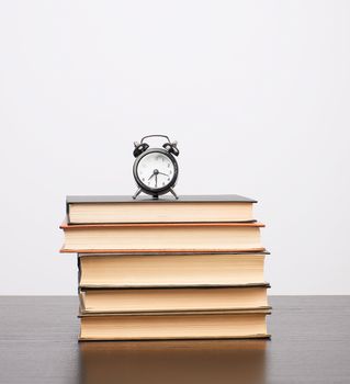 stack of books and a black alarm clock on the table, white background, copy space