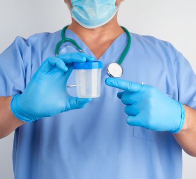 doctor in blue uniform and latex gloves is holding an empty plastic container for taking urine samples, close up
