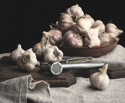 raw unpeeled garlic on a very old vintage cutting board and iron press, dark background