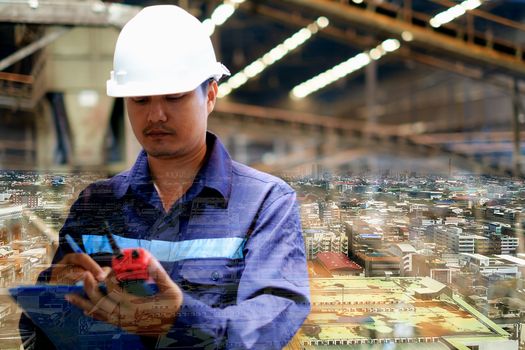 Double exposure of city background and engineer with uniform and white safety helmet working in the production line process plant, industrial concept