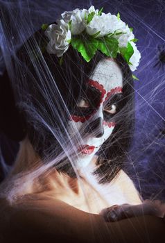 Young beautiful girl with traditional mexican death mask. Calavera Catrina. Sugar skull makeup. girl dressed in a wreath of white roses on a background of white web