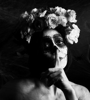 beautiful girl with traditional mexican death mask. Calavera Catrina. Sugar skull makeup. girl dressed in a wreath of roses, index finger attached to lips, black and white tinting