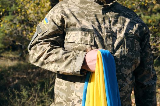 Ukrainian soldier holds in his hand the yellow-blue flag of the state, he pressed his hand to his chest, concept of the memory of the dead soldiers