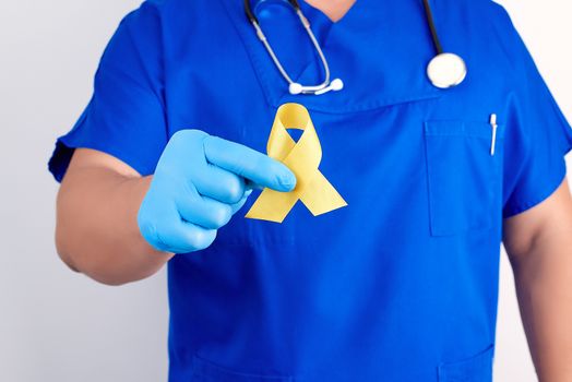 doctor in a blue uniform and sterile latex gloves holds a yellow ribbon in his hand, symbol of the fight against the cat's tumor, problem of suicides and their prevention, close up