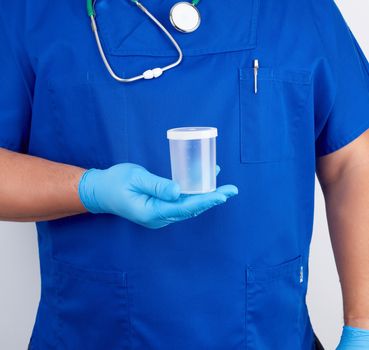 doctor in blue uniform and latex gloves is holding an empty plastic container for taking urine samples, concept of timely diagnosis