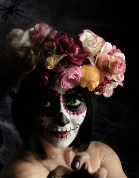 girl with black hair is dressed in a wreath of multi-colored roses and makeup is made on her face Sugar skull to the day of the Dead, close up