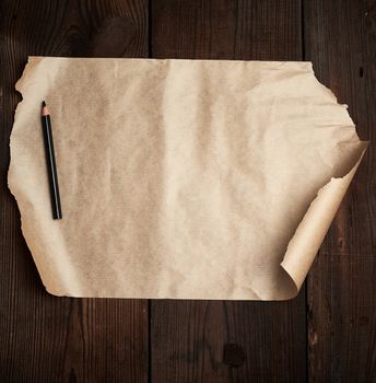 torn empty sheet of brown paper and a black pencil on a wooden surface from old boards, copy space