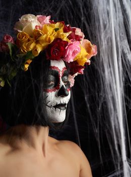 Young beautiful girl with traditional mexican death mask. Calavera Catrina. Sugar skull makeup. girl dressed in a wreath of roses on a background of white web