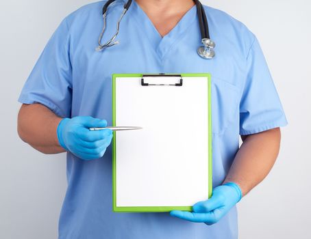doctor in blue uniform and latex gloves holds a green holder for sheets of paper and with a metal pen shows on a sheet, white background