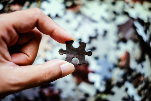 Hand holding Jigsaw with blurred pieces of puzzle background