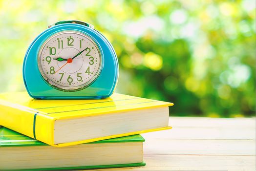 Old blue alarm clock on books with blurred green natural background
