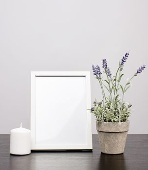 empty white frame, flowerpot with flower and candle on a black table, white background