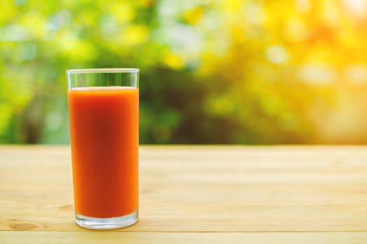 A glass of tomato juice on wooden table with blurred natural green background
