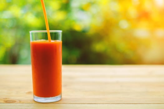 Pouring tomato juice into a glass on wooden table with blurred natural green background