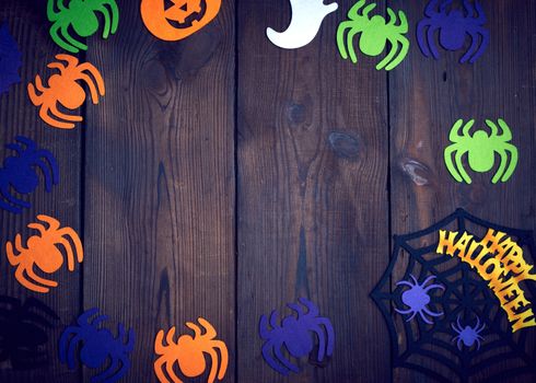 multicolored felt spider figures, cobweb on brown wooden background, holiday backdrop for Halloween