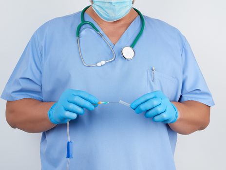 doctor in blue uniform and latex gloves holds a plastic system for intravenous droppers, white background