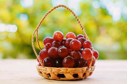 Red grape fruit in the basket on the wooden table with the natural blurred background
