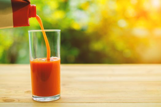 Pouring tomato juice into a glass on wooden table with blurred natural green background