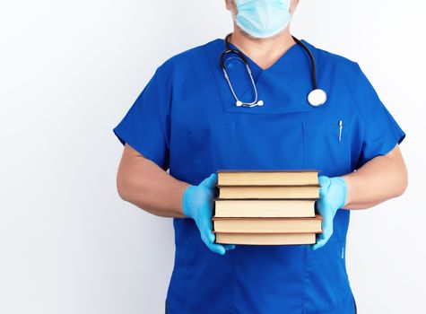 doctor in blue uniform and sterile latex gloves holds a stack of books in his hand against a gray background,  man stands in front