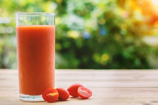 A glass of tomato juice on wooden table with blurred natural green background