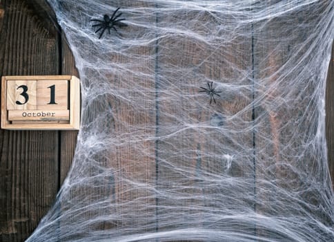 White spider web and wooden retro calendar made of blocks with the date of October 31, backdrop for Halloween holiday