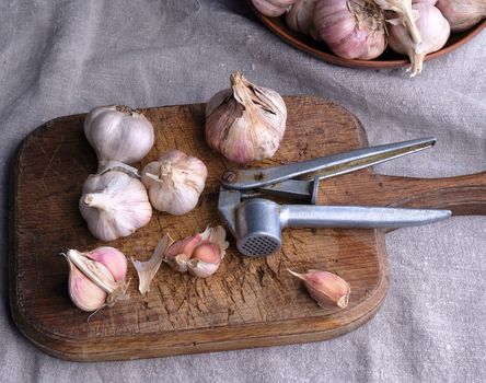 raw unpeeled garlic on a very old vintage cutting board and an iron extruder for a product, dark background