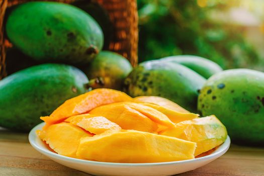 Ripe mango fruit in the basket on wooden table with blurred green background, selective focus