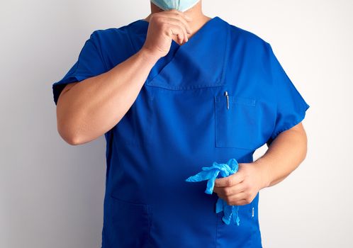 doctor in blue uniform holds sterile latex gloves and puts on a mask, white background