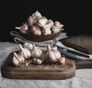raw unpeeled garlic on a very old vintage cutting board and iron pres, dark background