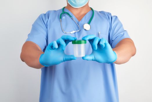 doctor in blue uniform and latex gloves is holding an empty plastic container for taking urine samples, concept of timely diagnosis