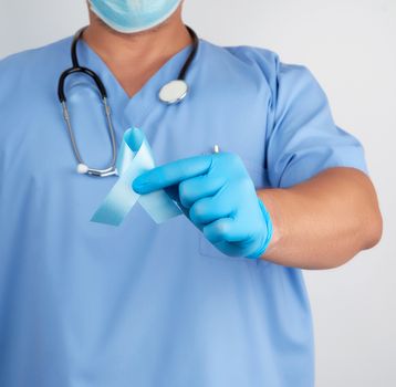 doctor in uniform and latex gloves holding a blue ribbon in his hand, symbol of the fight and treatment of prostate cancer