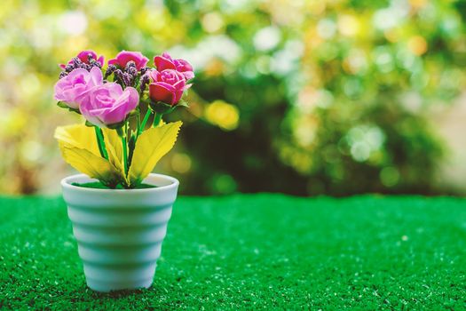Artificial flower in flowerpot on green grass with blurred natural background