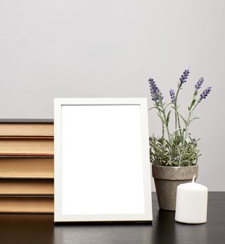 empty white photo frame, stack of books and a pot of growing lavender on a black table