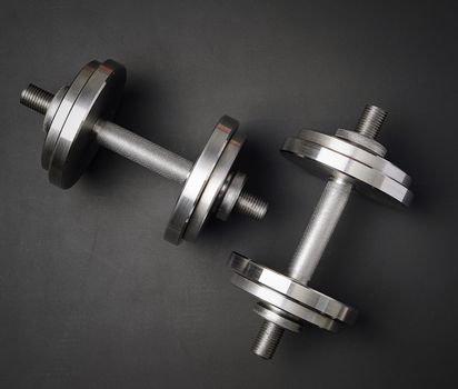 pair of shiny steel typesetting dumbbells for bodybuilding on a black background, top view