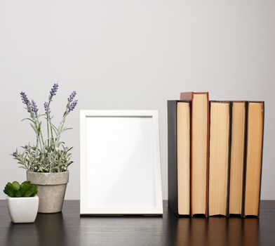 empty white photo frame, stack of books and a pot of growing lavender on a black table, workplace 