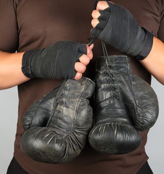 athlete in brown clothes holds very old black vintage leather boxing gloves, white background, close up 