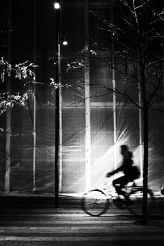 High contrast image of silhouette of man bicycling in motion blur in urban environment.