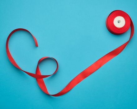 curled red satin ribbon on blue background, flat lay