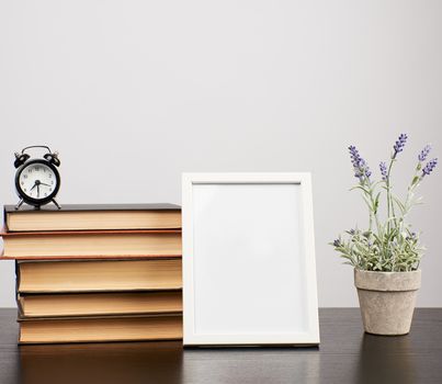 empty white photo frame, stack of books and a pot of growing lavender on a black table