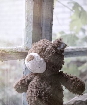 brown teddy bear sits on a windowsill and looks out the window, nostalgia concept