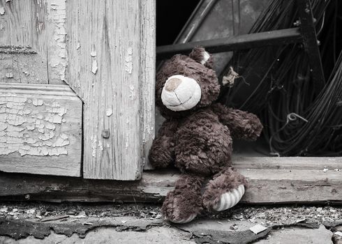 little teddy bear sits on the doorstep near an old door with cracked paint, concept of depression and nostalgia