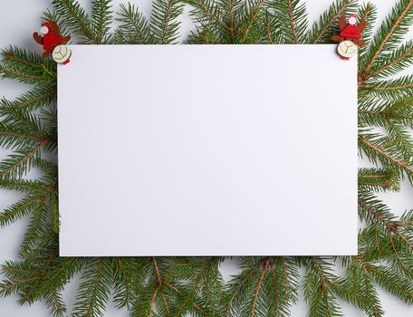 congratulatory Christmas background with an empty white sheet and green branches of spruce decorated with holiday toys on a white background, mock up 