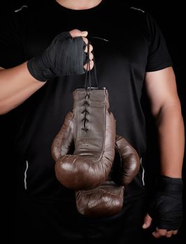 athlete in black clothes holds very old vintage leather brown boxing gloves, low key